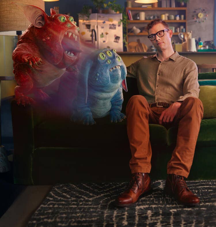 Man seated on couch with an illustrated depiction of a creature